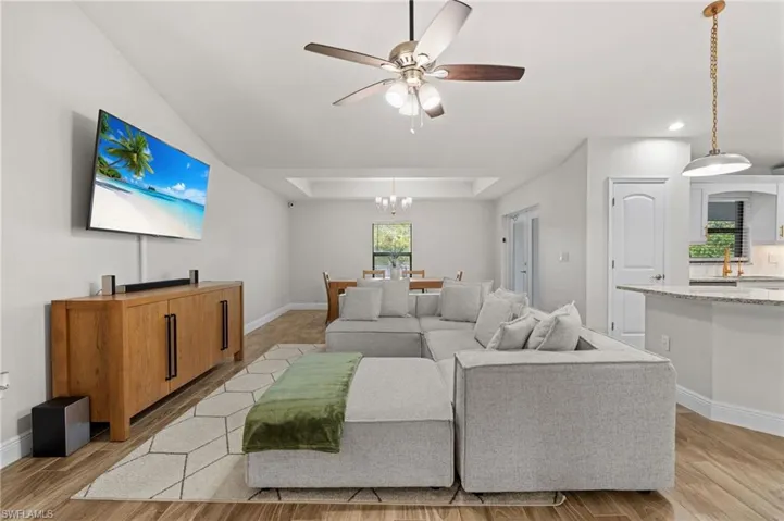 Living room with ceiling fan with notable chandelier, light hardwood / wood-style floors, and a raised ceiling