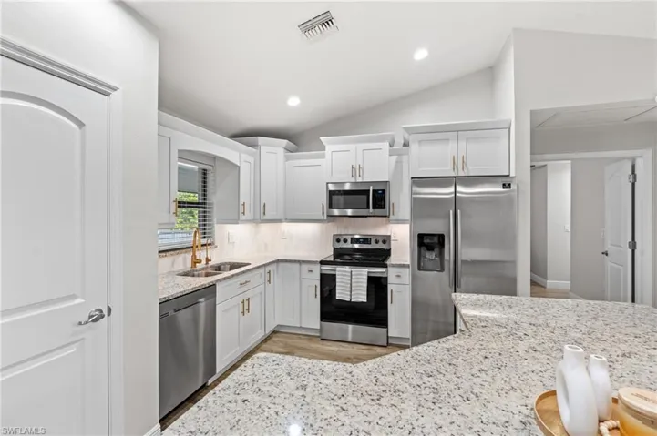 Kitchen with decorative backsplash, stainless steel appliances, white cabinetry, and lofted ceiling