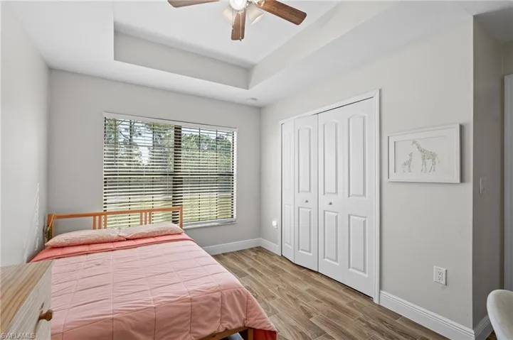 Bedroom with a raised ceiling, ceiling fan, a closet, and hardwood / wood-style floors