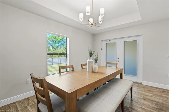 Dining area with french doors, light wood-type flooring, a tray ceiling, and a notable chandelier