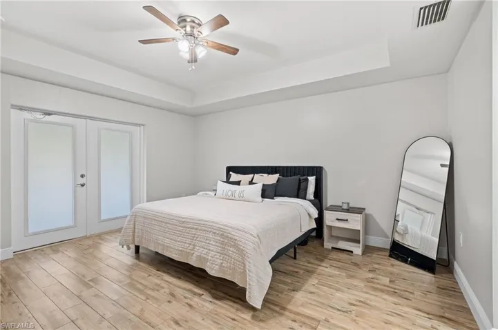 Bedroom featuring a raised ceiling, ceiling fan, french doors, and light wood-type flooring