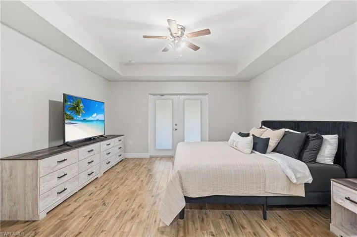 Bedroom featuring ceiling fan, a raised ceiling, light hardwood / wood-style flooring, and french doors