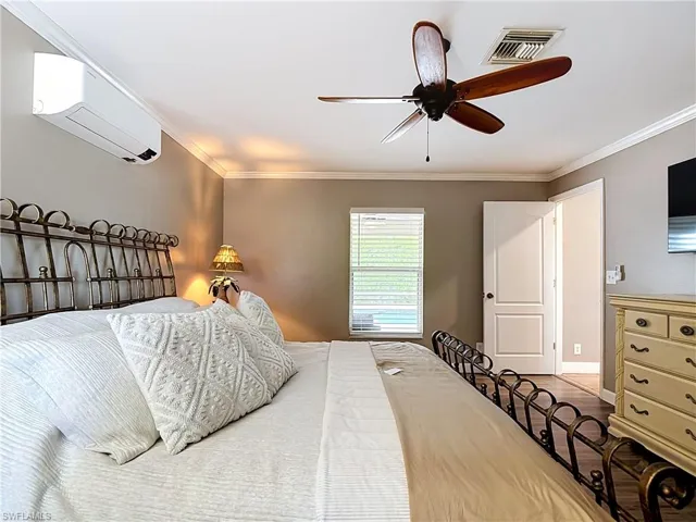 Bedroom featuring a wall-mounted mini-split system and a ceiling fan with wood-finish blades