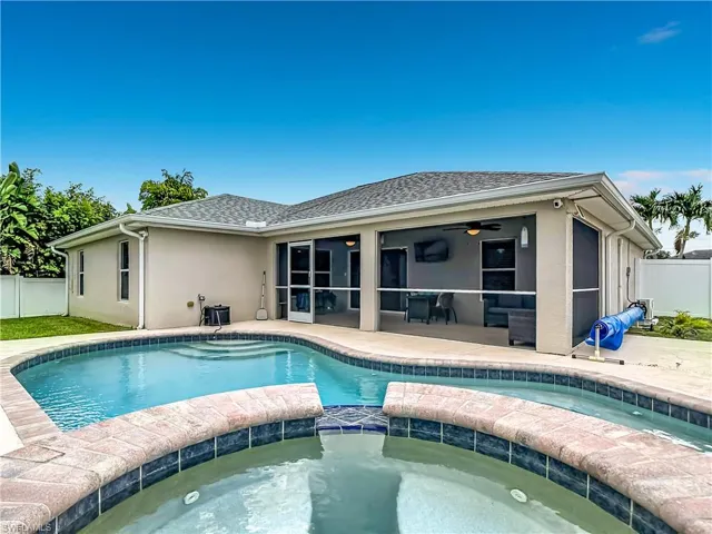 Exterior featuring a curved swimming pool with integrated spa, a screened-in patio, and a light-colored stucco finish