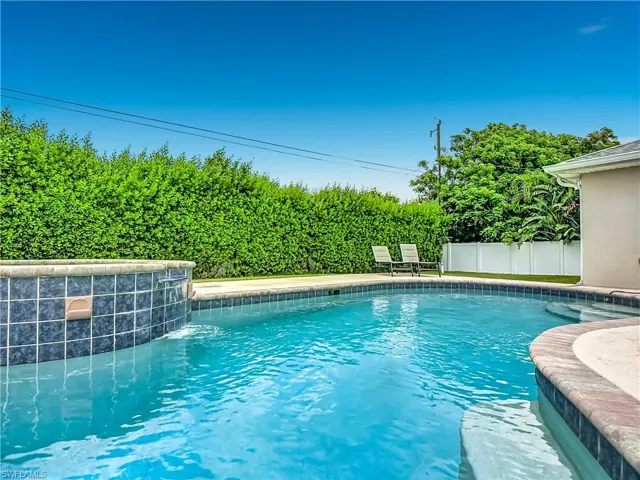 In-ground swimming pool with an integrated spa, featuring blue tile accents and a stone coping