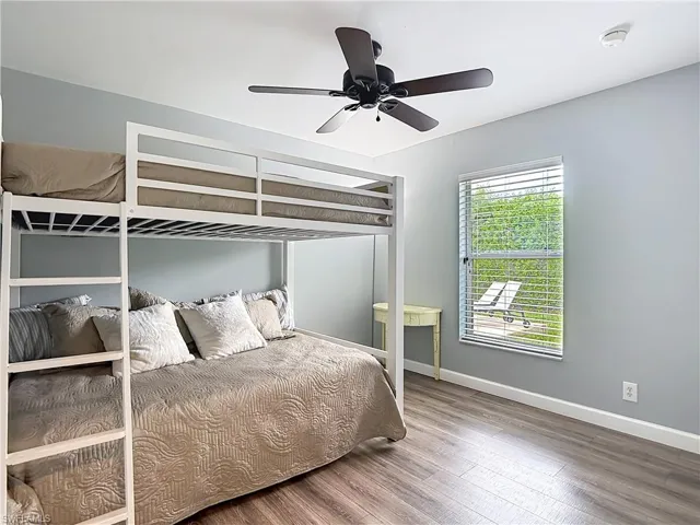 Room featuring wood-finish flooring, light gray walls, a window with horizontal blinds, and a dark-toned ceiling fan