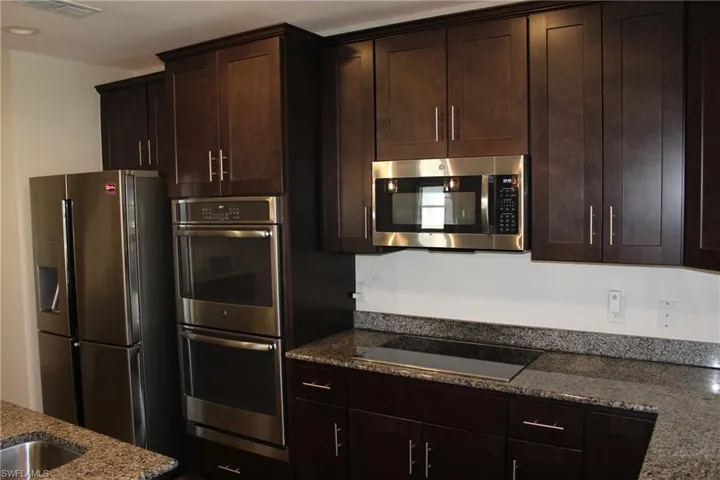 Kitchen featuring dark brown cabinetry, appliances with stainless steel finishes, and stone countertops