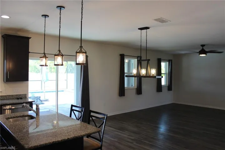 Kitchen with dark stone counters, dark wood-type flooring, ceiling fan, pendant lighting, and sink