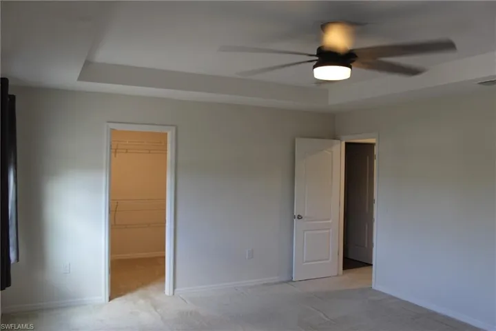 Unfurnished bedroom with a closet, ceiling fan, a walk in closet, light carpet, and a raised ceiling