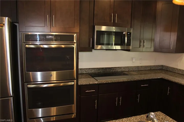 Kitchen featuring dark stone counters, dark brown cabinetry, and appliances with stainless steel finishes