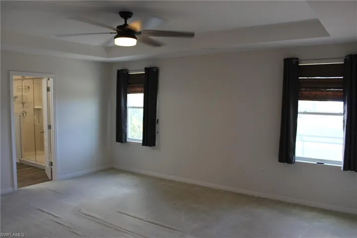 Empty room with carpet, ceiling fan, and a raised ceiling