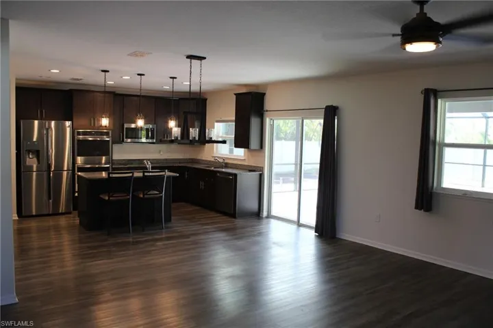 Kitchen featuring stainless steel appliances, dark vinyl flooring, a kitchen island, and pendant lighting