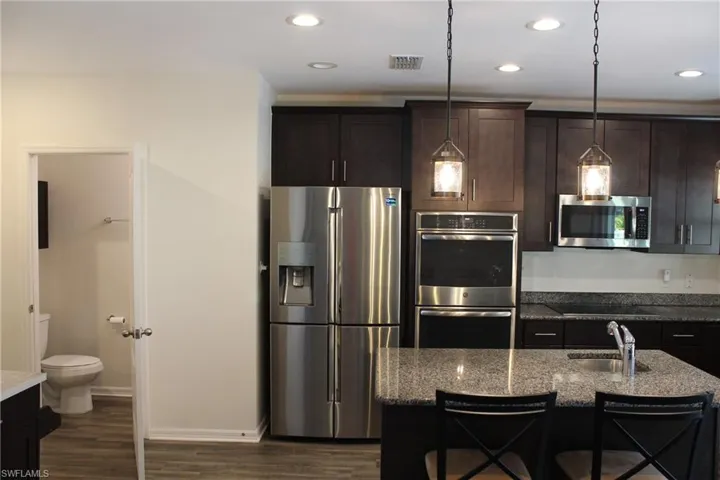 Kitchen featuring sink, light stone countertops, dark hardwood / wood-style floors, appliances with stainless steel finishes, and a kitchen breakfast bar