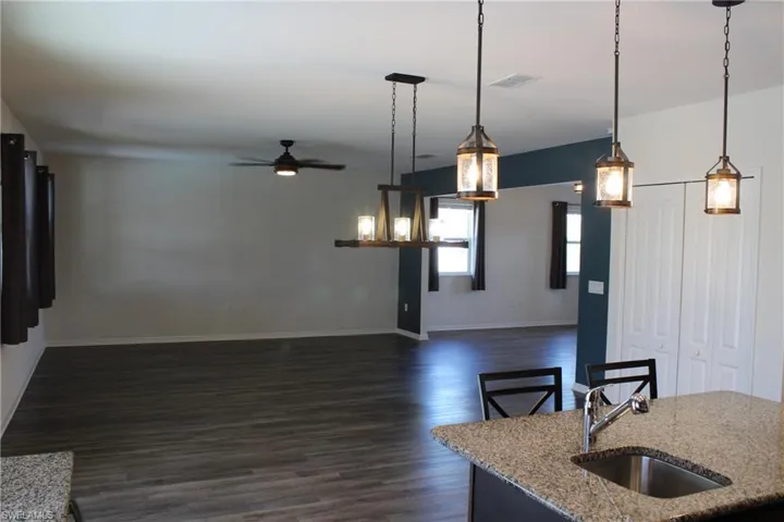 Kitchen with ceiling fan, hanging light fixtures, dark hardwood / wood-style flooring, sink, and light stone countertops
