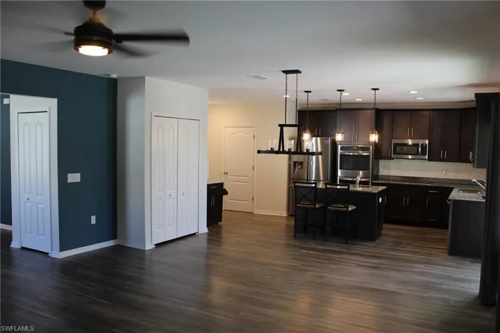 Kitchen with appliances with stainless steel finishes, decorative light fixtures, a kitchen island with sink, dark vinyl style floors, and ceiling fan