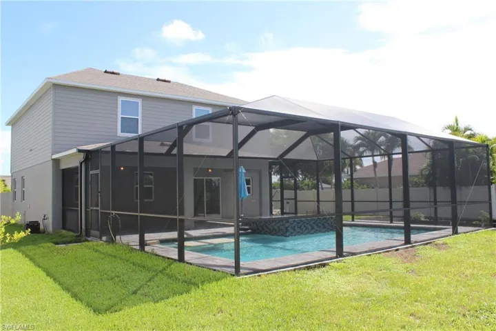 Rear view of property featuring glass enclosure, a lawn, and a fenced in pool