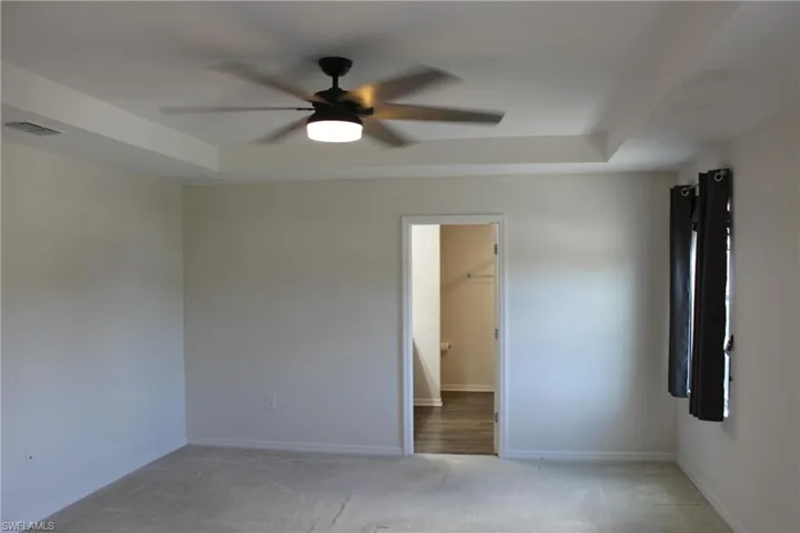 Unfurnished bedroom featuring a tray ceiling, carpet, ceiling fan, and a walk in closet