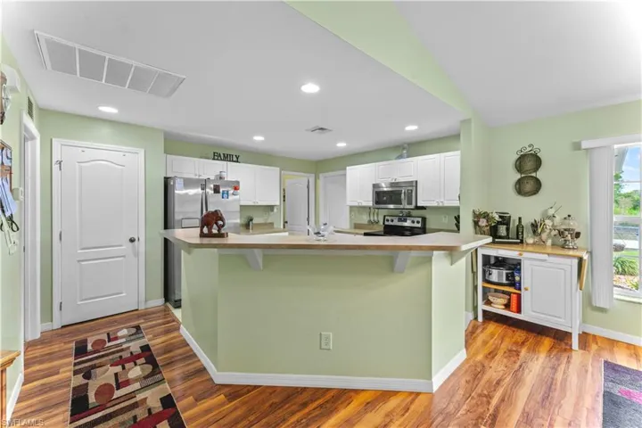 Kitchen featuring white cabinets, appliances with stainless steel finishes, hardwood / wood-style flooring, and a kitchen bar