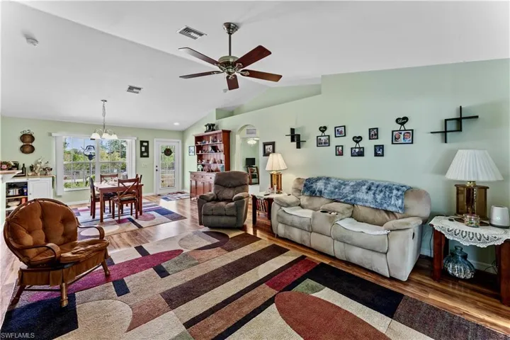 Living room with lofted ceiling, ceiling fan with notable chandelier, and hardwood / wood-style flooring