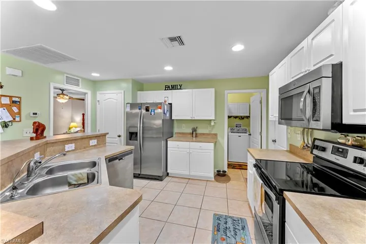 Kitchen with sink, white cabinetry, stainless steel appliances, and washer / dryer