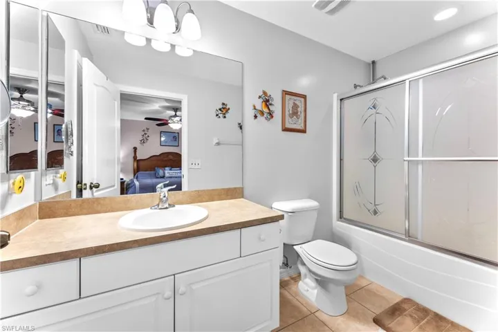 Full bathroom with tile flooring, ceiling fan, oversized vanity, enclosed tub / shower combo, and toilet