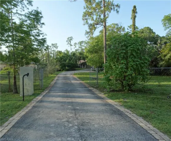 View of asphalt driveway featuring a gated entry and lots of guest parking