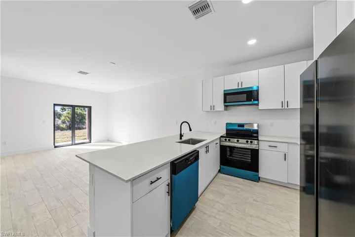Kitchen with freestanding refrigerator, stainless steel range with electric cooktop, a peninsula, white cabinets, and recessed lighting