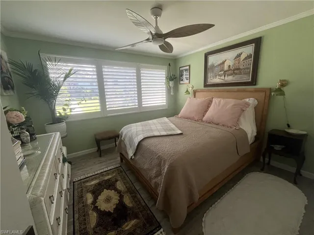 Bedroom featuring a ceiling fan, wood-finish flooring, and white plantation shutters over a multi-pane window