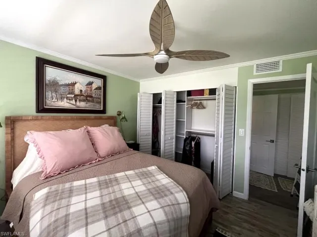 Bedroom featuring wood-finish flooring, a ceiling fan with leaf-shaped blades, crown molding, double bi-fold closet doors, and built-in closet shelving