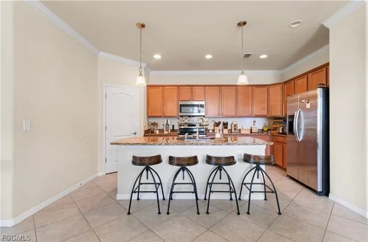 Kitchen featuring stainless steel appliances, light stone countertops, a kitchen island with sink, hanging light fixtures, and ornamental molding