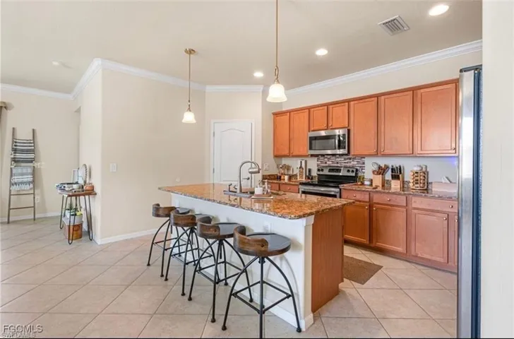 Kitchen with dark stone countertops, a breakfast bar, stainless steel appliances, an island with sink, and hanging light fixtures