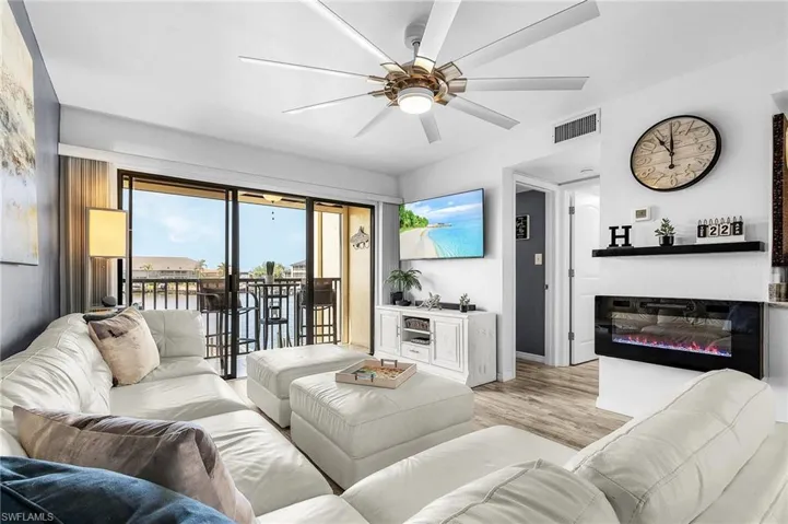 Living area with light wood finished floors, a glass covered fireplace, baseboards, visible vents, and ceiling fan