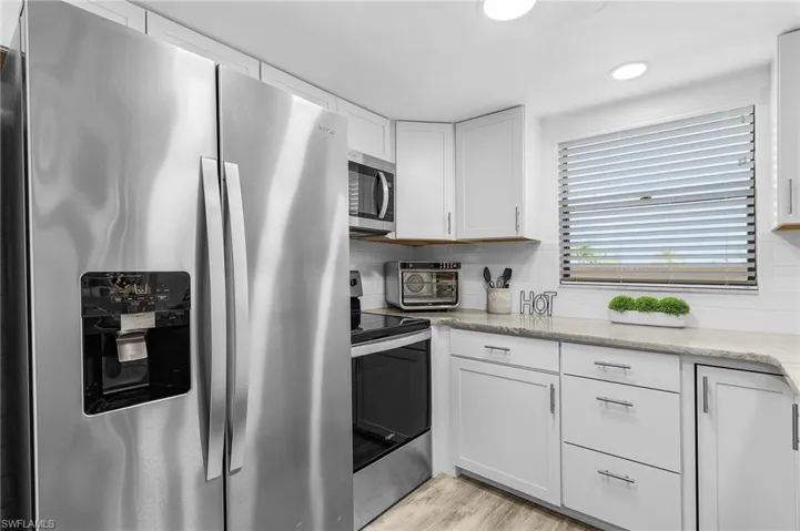 Kitchen with stainless steel appliances, light wood-style floors, white cabinetry, decorative backsplash, and light stone countertops