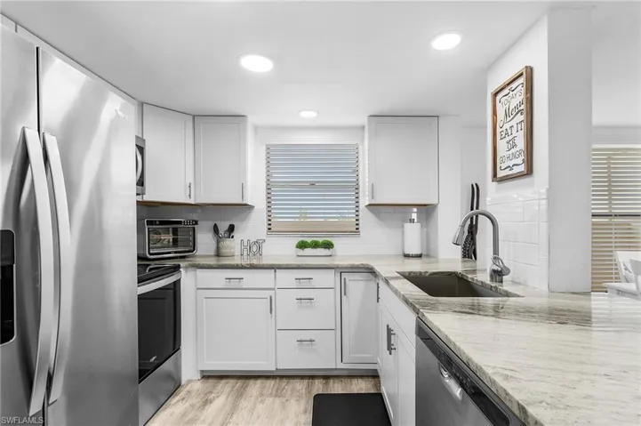 Kitchen with light stone countertops, stainless steel appliances, a sink, and backsplash