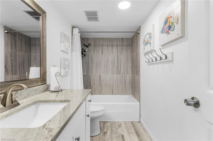 Bathroom with shower / bath combination with curtain, wood finished floors, visible vents, toilet, and vanity