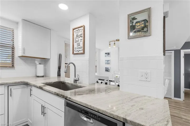 Kitchen with stainless steel dishwasher, a sink, light wood-type flooring, light stone countertops, and white cabinetry