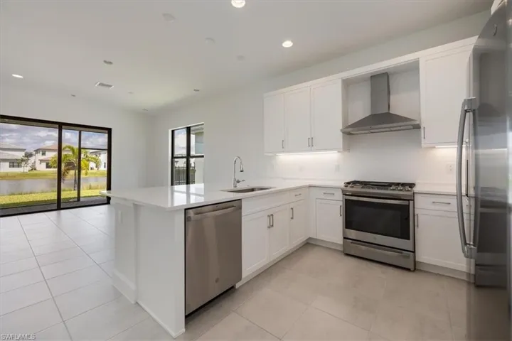 Kitchen with light tile patterned floors, stainless steel appliances, sink, wall chimney range hood, and kitchen peninsula