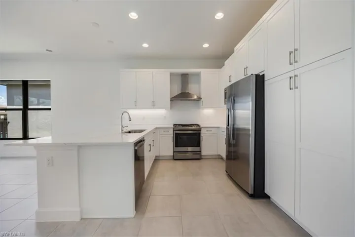 Kitchen featuring kitchen peninsula, sink, appliances with stainless steel finishes, light tile patterned flooring, and wall chimney range hood
