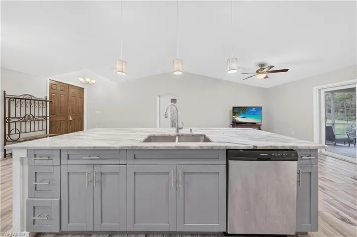 Kitchen island featuring stone-finish countertops, dual-basin stainless steel undermount sink, grey shaker-style cabinetry, stainless steel dishwasher, and three pendant lights