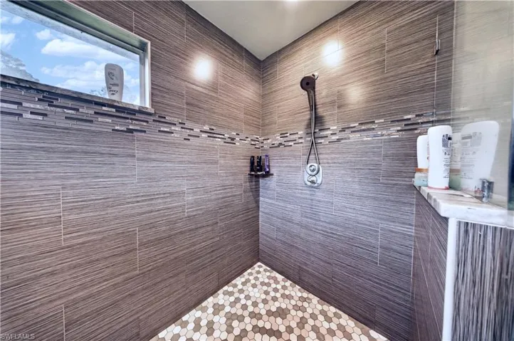 Walk-in shower featuring large-format horizontal wall tiling, decorative mosaic tile accents, hexagonal floor tile, a handheld shower fixture, and an integrated corner shelf