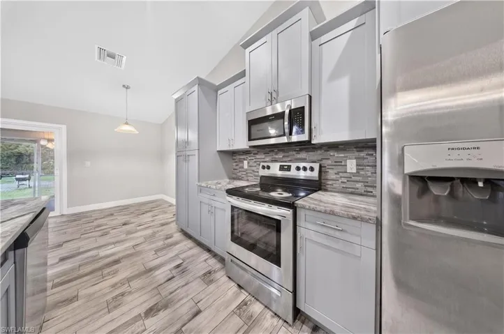 Kitchen featuring light gray cabinetry, stainless steel appliances, multi-tonal tile backsplash, wood-finish flooring, and vaulted ceilings