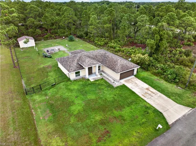 Single-story residence featuring a shingle roof, concrete driveway, attached garage, detached storage structure, and fenced perimeter
