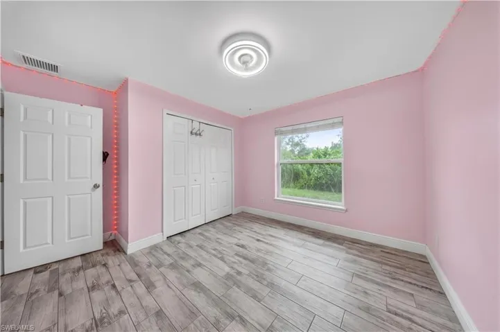 Room featuring wood-finish tile flooring, a dual-panel closet, a single-pane window, and a modern circular flush-mount ceiling light fixture