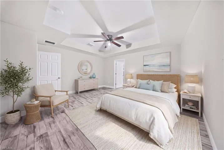 Tray ceiling with a central multi-blade ceiling fan and wood-finish flooring