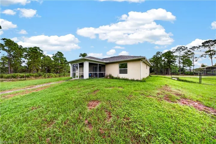 Stucco exterior featuring a screened lanai, hip roof, and expansive lot with mature trees