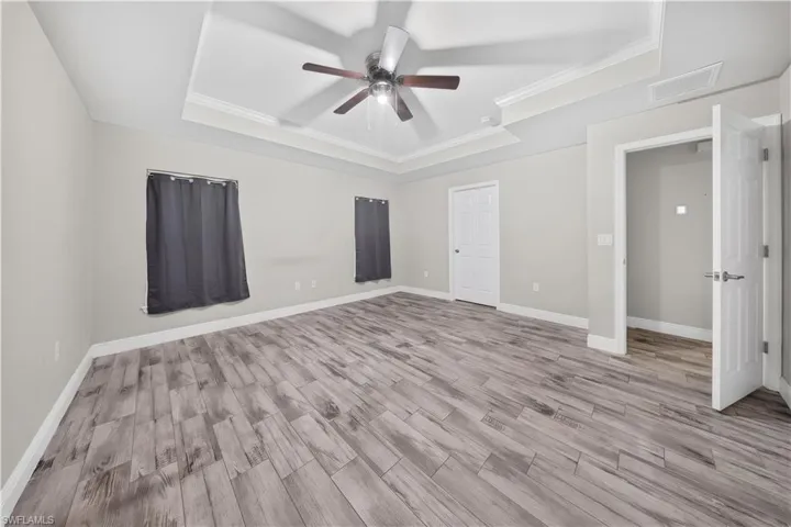 Room featuring wood-finish flooring, tray ceiling, and a central ceiling fan with integrated light fixture