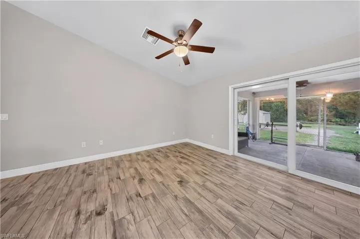 Room featuring wood-finish tile flooring, vaulted ceiling, central ceiling fan with integrated lighting, and large sliding glass doors opening to a covered patio