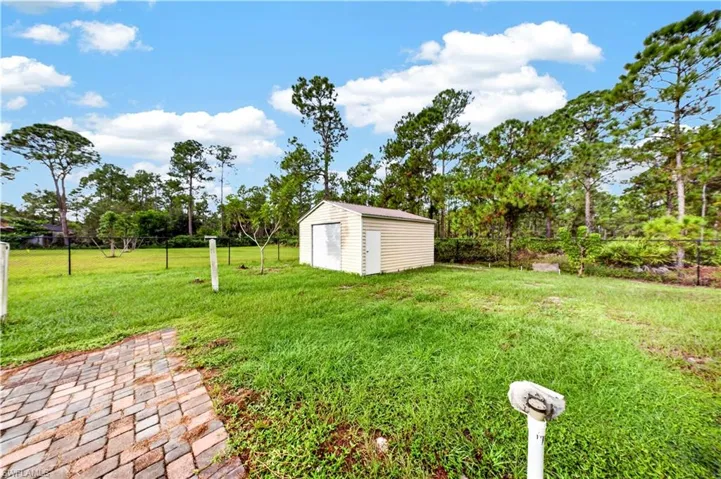 Expansive backyard featuring a detached storage building, paver hardscaping, perimeter fencing, and mature trees