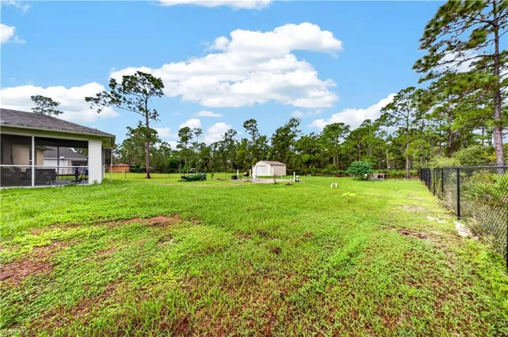 Expansive backyard featuring a grass lawn, screened-in porch, metal chain-link perimeter fencing, and a detached storage structure