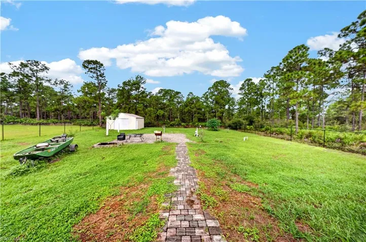 Expansive backyard featuring a stone paver walkway, detached storage building, metal perimeter fencing, and mature trees